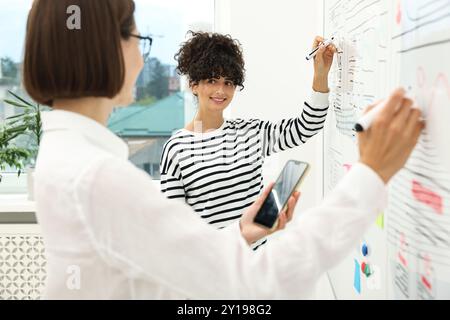Developing UI design. Women drawing website wireframe on whiteboard indoors Stock Photo