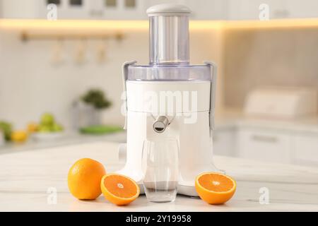 Modern juicer, oranges and glass on white marble table in kitchen Stock Photo