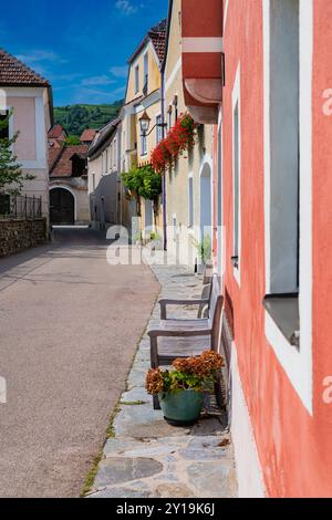 rightly colored historic houses with a wooden bench in the foreground decorated with red flowers along a narrow street in Weißenkirchen World Heritage Stock Photo