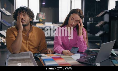 Two designers male female colleagues in modern design studio looking at fabric samples discussing color textile for interior angry Arabian Indian man Stock Photo