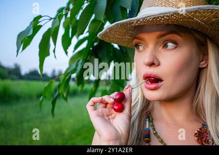 A woman holding a cherry in her mouth, looking sideways Stock Photo