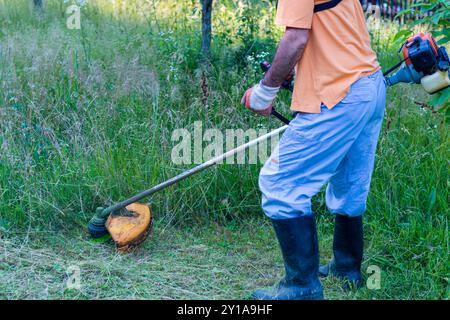 A mature man in protective clothing, and gloves with a trimmer. Mowing tall grass and the weeds with a trimmer. Selectively focus Stock Photo