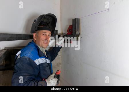 An experienced man   using a spirit level and welds a seam on a spiral staircase at a construction site. Stock Photo