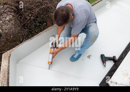 Man using sealant gun at roofing construction. Construction worker with silicone tube making roof waterproof Stock Photo