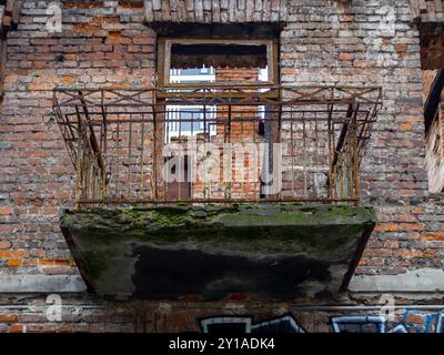 Made of red brick facade of an old tenement with balcony with rusty balustrade. Stock Photo