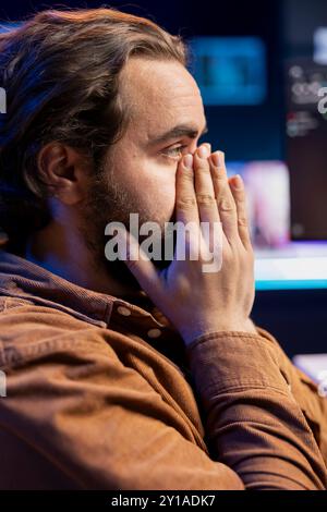 Worried cybersecurity expert putting face in hands after finding many security vulnerabilities, scared of malware infections. Anxious developer distressed by cyber attacks on computer systems Stock Photo