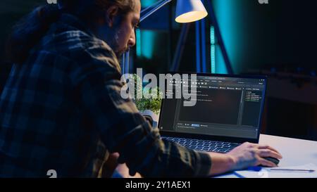 Skilled computer scientist writes code on laptop screen while in living room office using programming languages. Self employed IT specialist working on fixing database errors from home, camera A Stock Photo