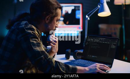 Experienced programmer writes code on laptop screen while in apartment office using Java programming languages. Developer remotely working on fixing database errors while working from home, camera A Stock Photo