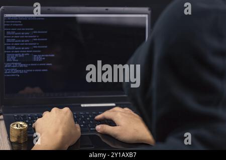 Dangerous hooded hacker on laptop breaks computer security sistem and steal bitcoin cryptocurrency Stock Photo