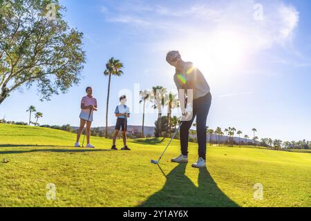 Full length low angle view photo of a male caucasian instructor teaching golf to two kids in a course Stock Photo