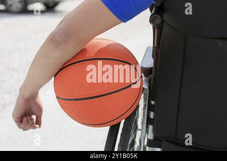 Disabled young basketball player on a wheelchair holding ball and beeing active in sport Stock Photo