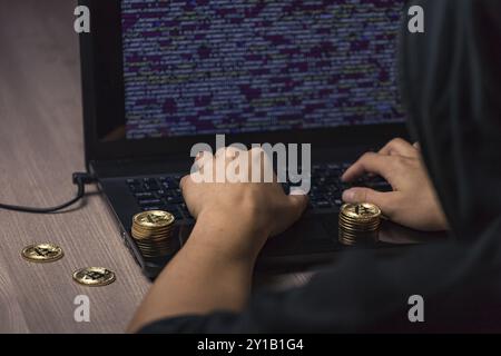Dangerous hooded hacker on laptop breaks computer security sistem and steal bitcoin cryptocurrency Stock Photo