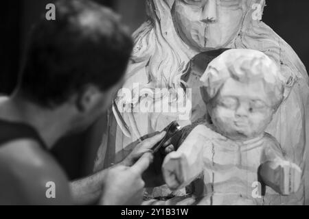 An artist focusing on carving details into a wooden sculpture, captured in black and white Stock Photo