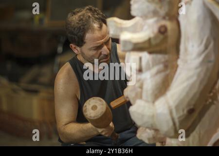 Man focused on carving wood with a mallet in a workshop, showcasing detailed artistry Stock Photo