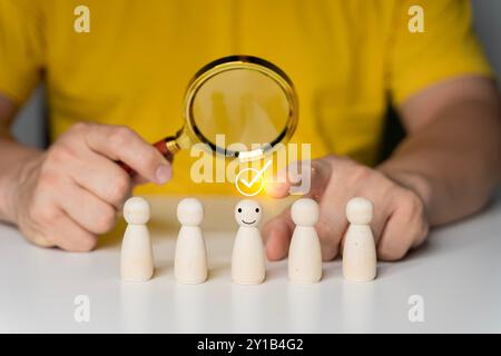 Human resource (HR), hiring, selection, recruitment, CRM, right people and unique concepts. Human Hand Holding Magnifying Glass Over Wooden Figures. Stock Photo