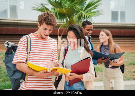 Two multiracial students review their class notes in a notebook while their classmates discuss the lesson learned at the high school. Group of teenagers reading a textbook on the university campus. High quality photo Stock Photo
