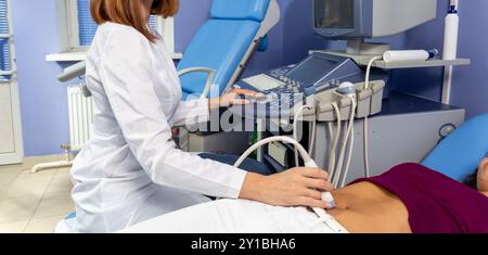 The doctor performs an ultrasound diagnosis of the abdominal cavity of a pregnant girl at an early stage of pregnancy. Ultrasound scanning of intestin Stock Photo