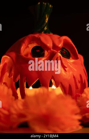 Vertical photo featuring a hollow Halloween pumpkin with candles inside, accompanied by a lit red candle and vibrant orange marigolds. All set on a bl Stock Photo