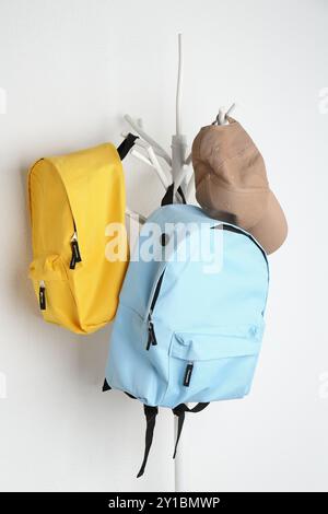 Bright backpacks and cap hanging on white wall Stock Photo