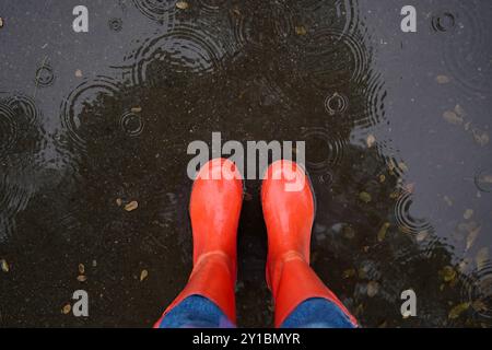 Woman wearing red rubber boots standing in rippled puddle, top view Stock Photo