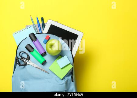 Light blue school backpack with stationery, apple and tablet on yellow background, top view. Space for text Stock Photo
