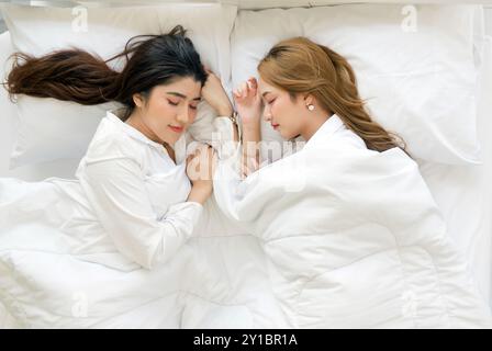 Young asian couple in white pajama, sleep and sweet dream lying on bed with soft pillow and a comfortable duvet wrapped around. Top view Stock Photo