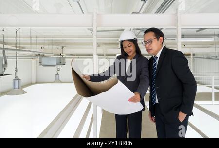 Engineer in hardhat hold the ventilation system construction plan while taking the building inspector check the cleanliness of the factory. Lighting a Stock Photo