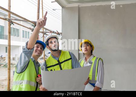 Young engineer in a construction helmet and safety vest explaining to foreman about the project that are under construction. Work environment of engin Stock Photo