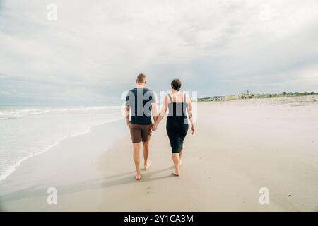 A couple walks hand-in-hand along a serene, overcast beach Stock Photo