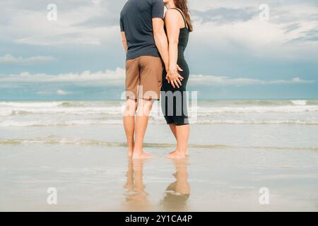 Couple standing on the beach, holding hands with reflection Stock Photo