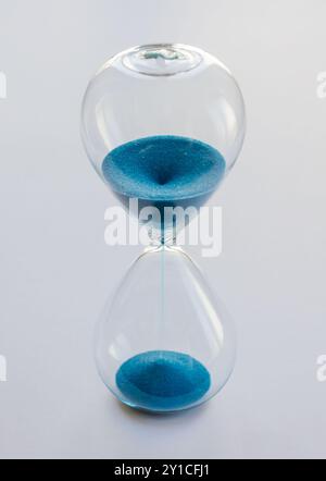 Hourglass containing blue sand isolated on white background. Concept of time passing Stock Photo
