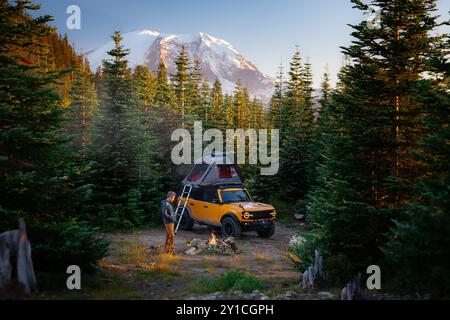 Yellow overlanding truck and man by firepit in forest near Mt. Rainier Stock Photo