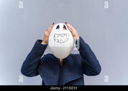 woman holding large balloon with jack-o-lantern face drawing in front of her own face Stock Photo