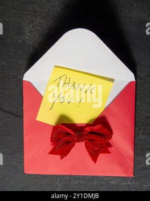 Yellow Thank You Adhesive Note on a red envelope and red bow on a slate background Stock Photo
