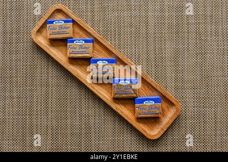 Kirkwall, Orkney, Scotland - July 15, 2024: Single serving pats of Meggle brand Feine Butter on a wooden serving tray. Stock Photo