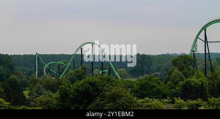 Netherlands, Biddinghuizen - July 15, 2014 - A green roller coaster with multiple loops and hills, set against a backdrop of trees and a cloudy sky. T Stock Photo