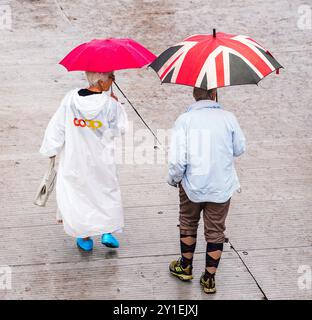 Goodwood Revival. Looking down on a couple in white raincoats and pink and a union flag (Jack) umbrella. Man has brown plus fours and vintage socks. Stock Photo