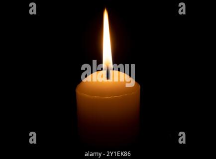 A single burning candle flame or light glowing on a big white candle is isolated on red or dark background on table in church for Christmas, funeral Stock Photo