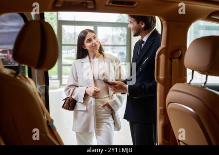 Shot from car cabin with beige leather interior of smiling well dressed woman consulting with auto dealer on buying new vehicle at dealership center Stock Photo