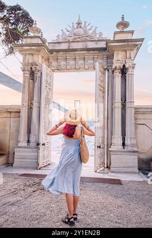 A happy young woman poses by the gate of a palace in Istanbul, enjoying her summer vacation with the Bosphorus in the background Stock Photo