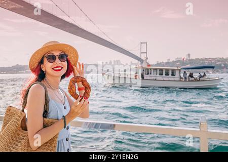 A Turkish woman enjoys a fresh simit by the Bosphorus in Istanbul, savoring the traditional sesame-covered snack on a summer day Stock Photo