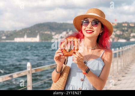 A woman holds a freshly baked simit, a traditional Turkish snack, while touring the scenic Bosphorus on a sunny summer afternoon in Istanbul Stock Photo