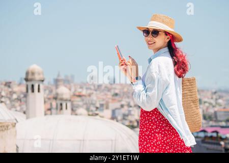 A stylish woman tourists in Istanbul, browsing her smartphone and checking a map while enjoying the sunny outdoor environment. Stock Photo