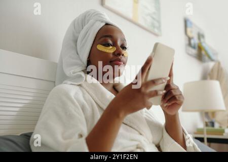 Woman Wearing Gold Eye Mask and Using Smartphone Relaxing Stock Photo