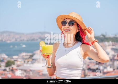 A young woman enjoying a refreshing cocktail on a rooftop terrace in Istanbul, overlooking the sea. Stock Photo