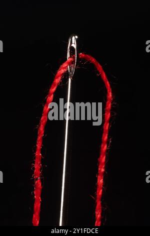 Macro of a red thread through the eye of a needle Stock Photo