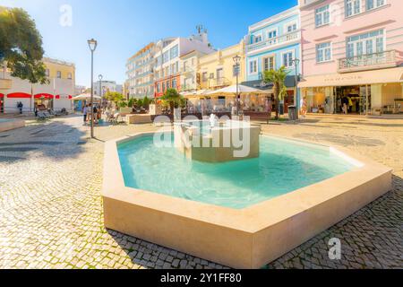 A picturesque square with water fountains, sidewalk cafes and shops in the historic old town of the whitewashed fishing village of Lagos, Portugal. Stock Photo