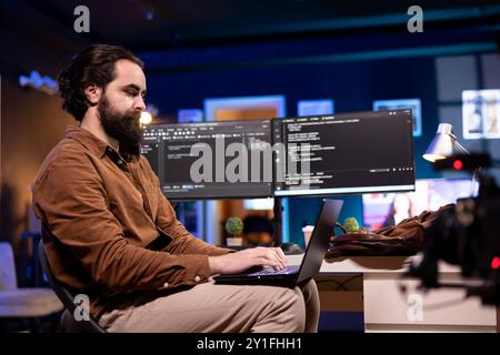 Programmer doing software debugging using laptop, checking errors in lines of code displayed on computer monitors. Man working from home fixing coding mistakes using notebook device Stock Photo