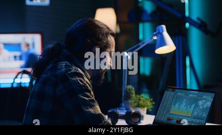 Smiling man satisfied about statistical data financial graphs on laptop screen while researching data. Remote worker happy about business graphic economic numbers, feeling pleased, camera A Stock Photo