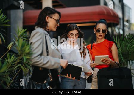 Three businesswomen collaborating outdoors on projects and discussing documents Stock Photo